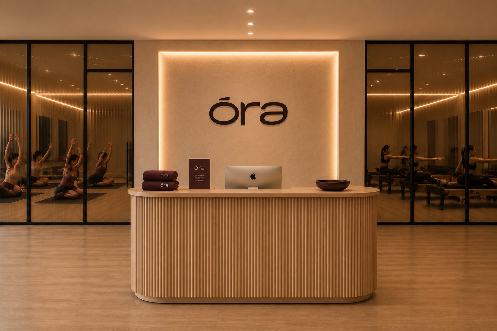 The ora studios reception: a curved fluted oak desk below the backlit ora wordmark, with glass walls on either side looking into the mat room and the reformer room.